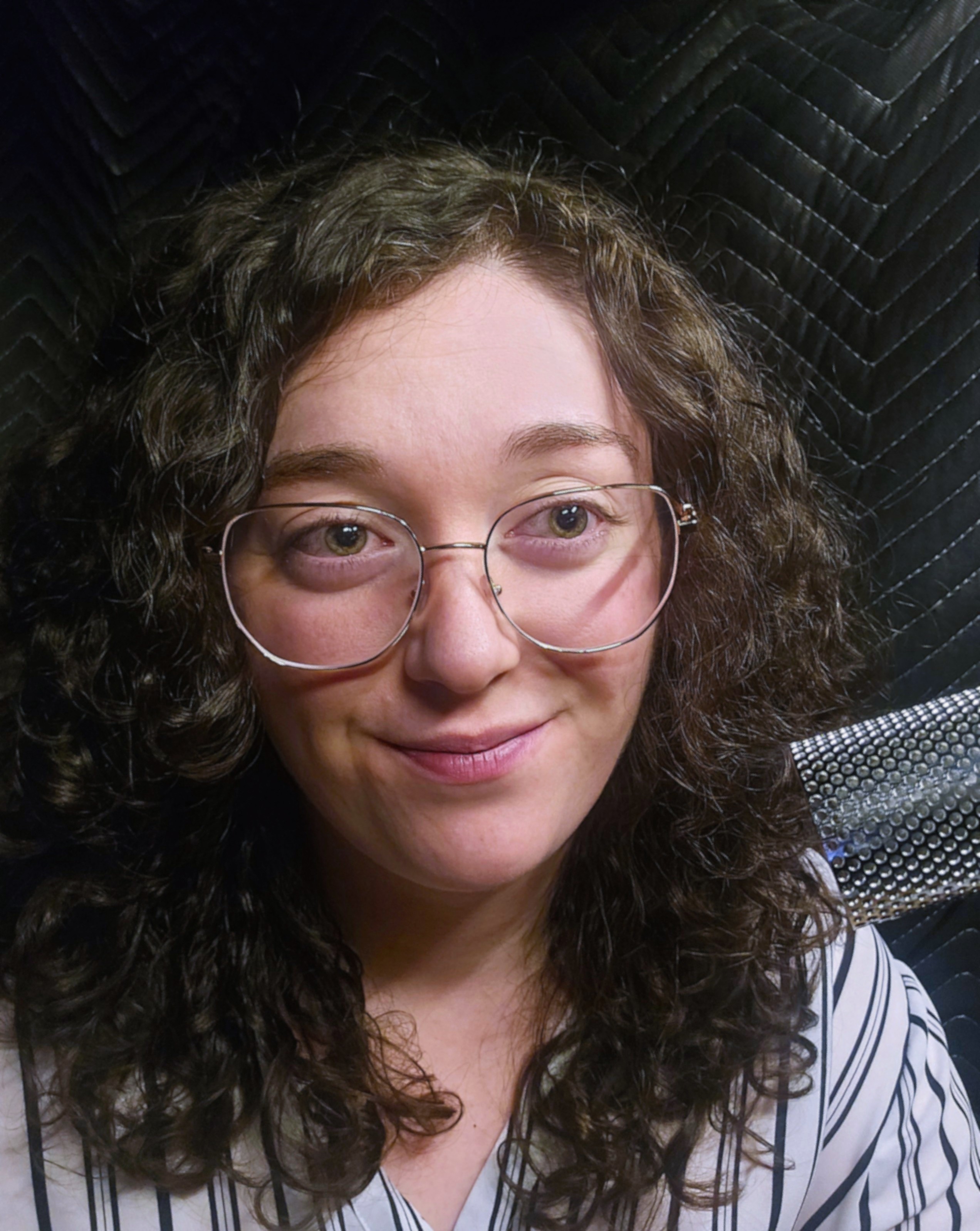 Selfie of Melissa in her booth, Headphones on, wearing glasses, standing in front of her microphone